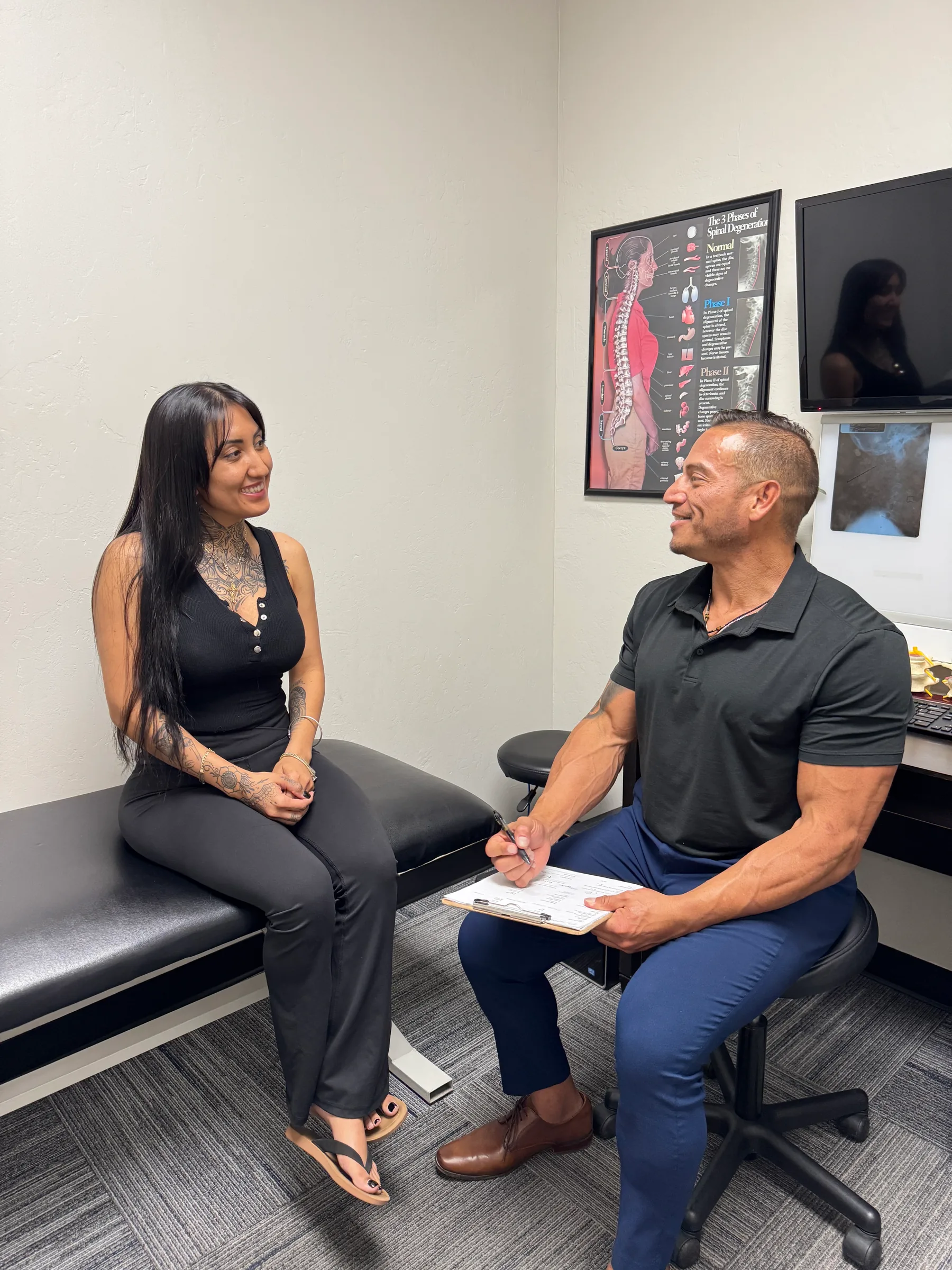 Chiropractor consulting with female patient in medical office exam room.