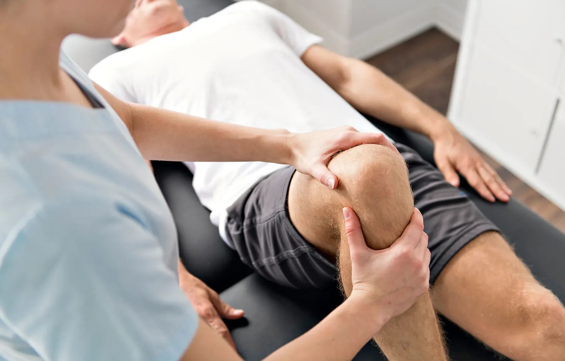 A chiropractor performs a knee examination and adjustment on a seated patient during a clinical assessment.
