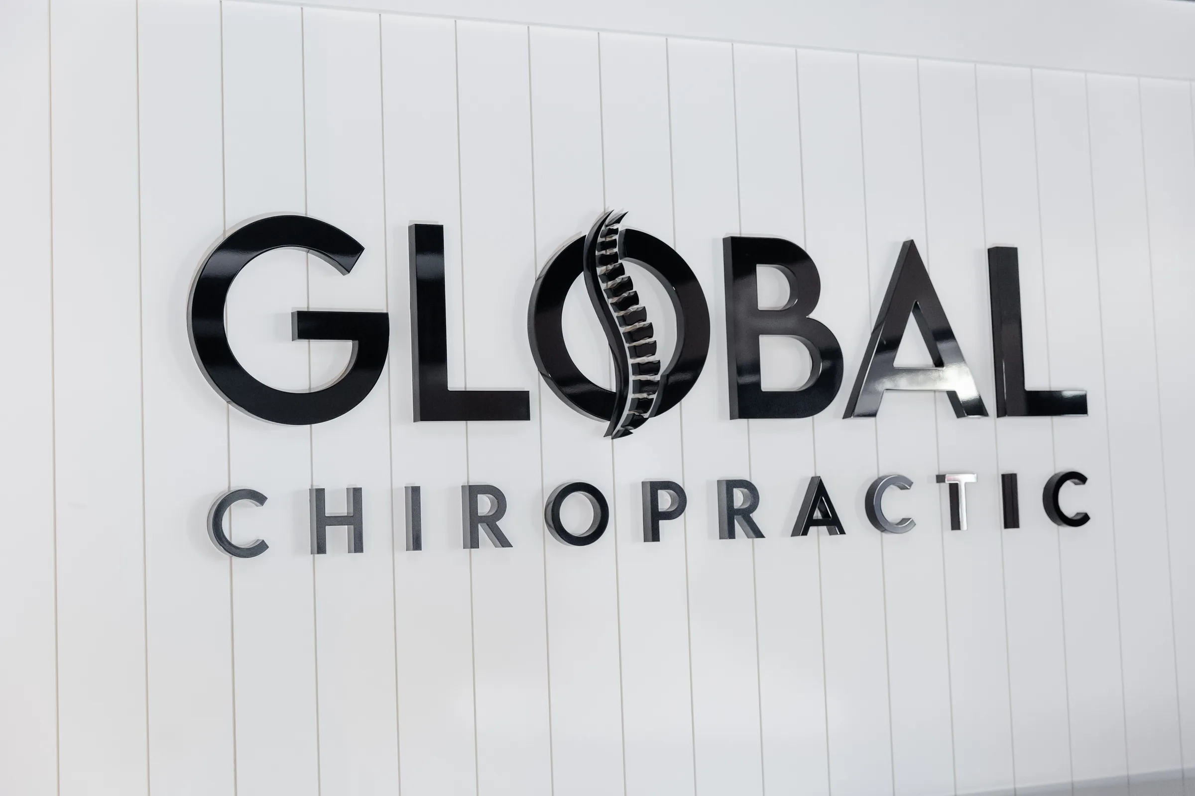 Global Chiropractic signage with black letters and spine logo on white wall.